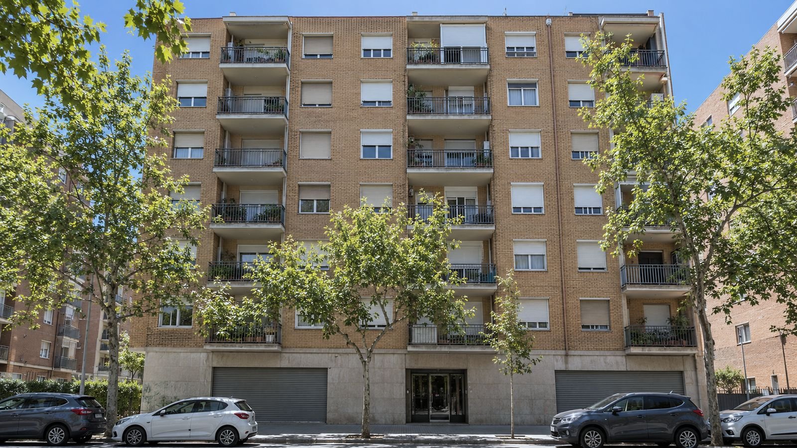 Bloque de pisos con persianas enrollables y balcones, visto desde la acera a media mañana